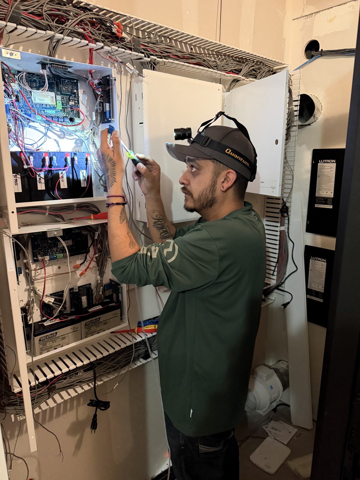 Technician with a headlamp servicing security panel boards and batteries